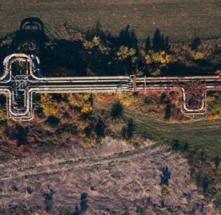 Aerial view of abandoned outdoor industrial heating pipeline. Top view of heat steam pipes through rural landscape from drone pov.