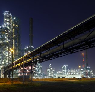 An oil refinery in the harbor of Antwerp with night blue sky, pipelines leading towards it.